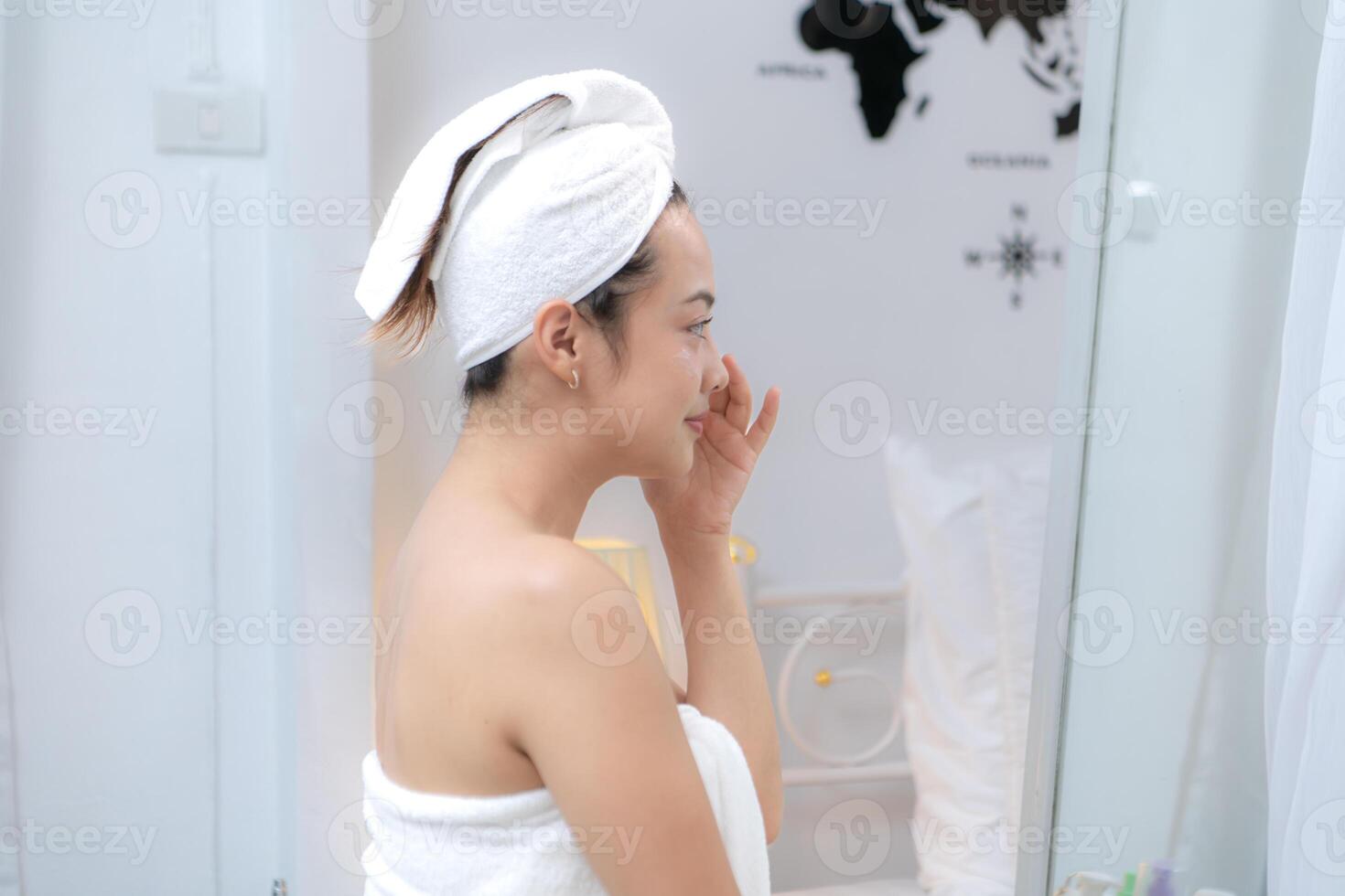 Asian young woman with towel wrapped on head and body applying makeup after shower, Morning beauty routine before work photo