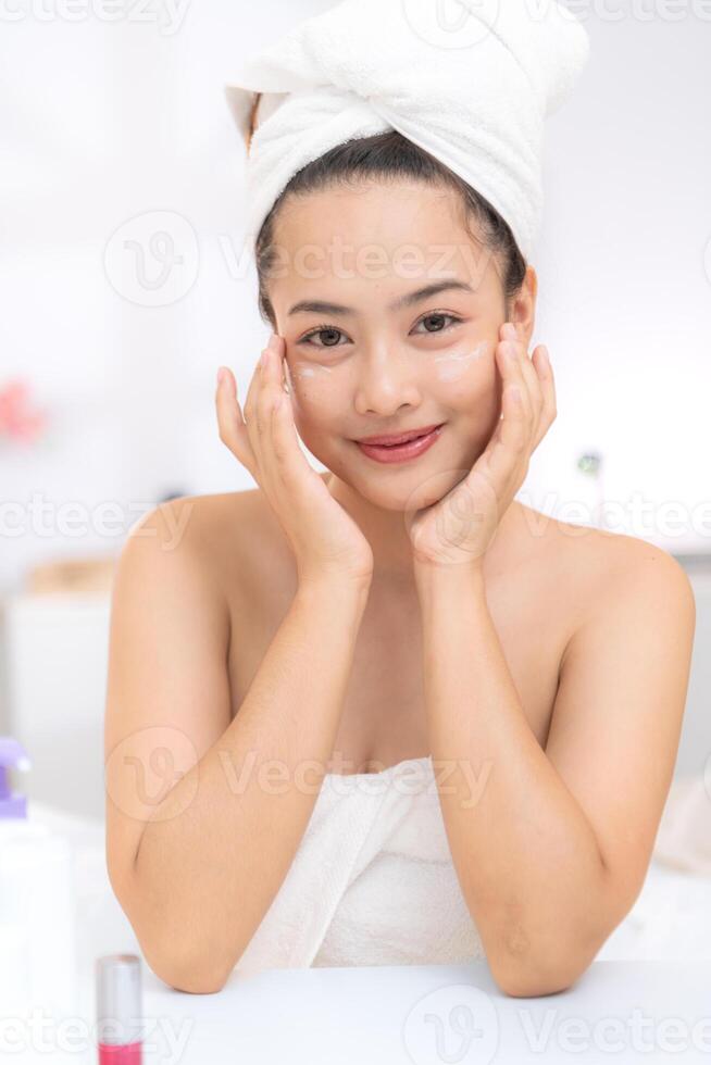 Asian young woman with towel wrapped on head and body applying makeup after shower, Morning beauty routine before work photo