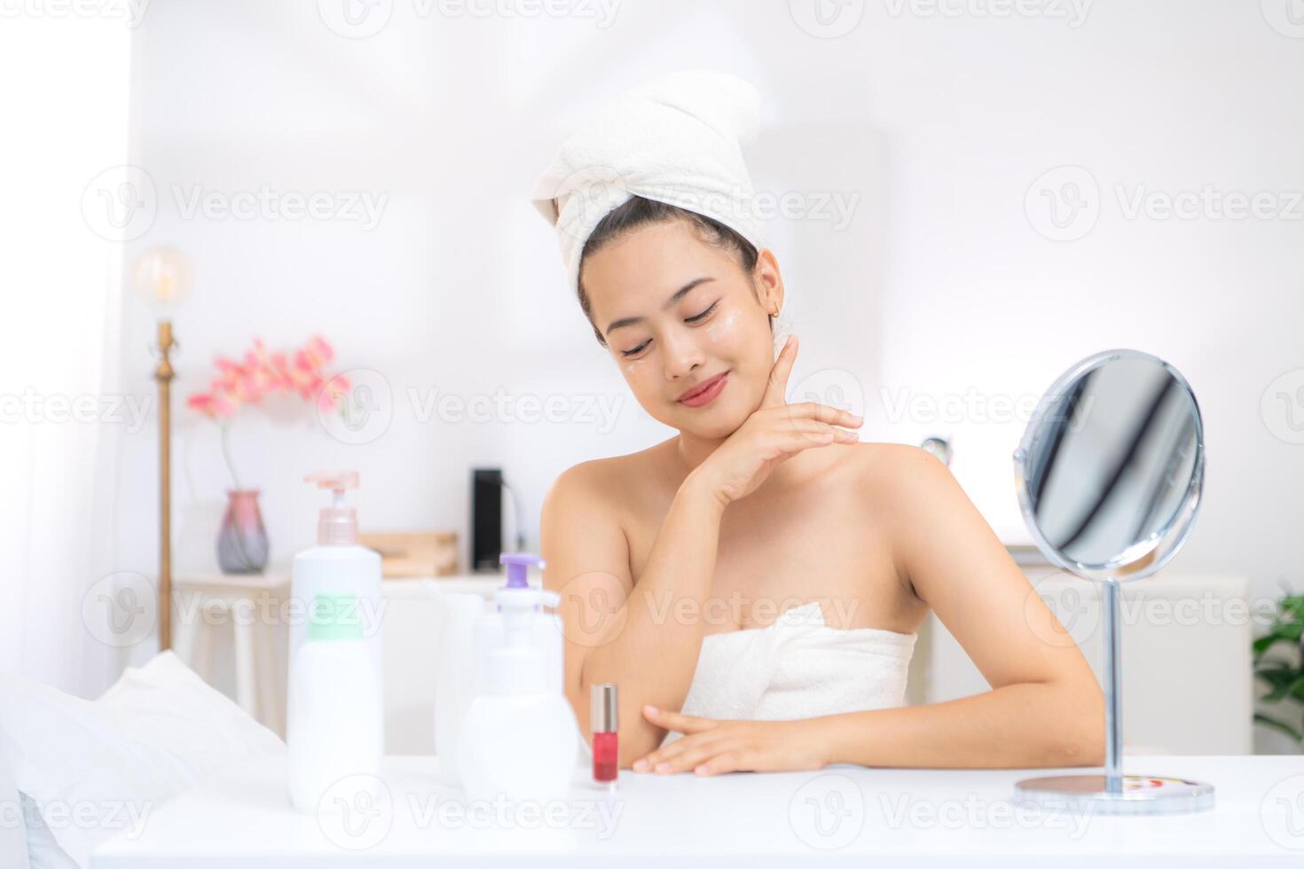Asian young woman with towel wrapped on head and body applying makeup after shower, Morning beauty routine before work photo