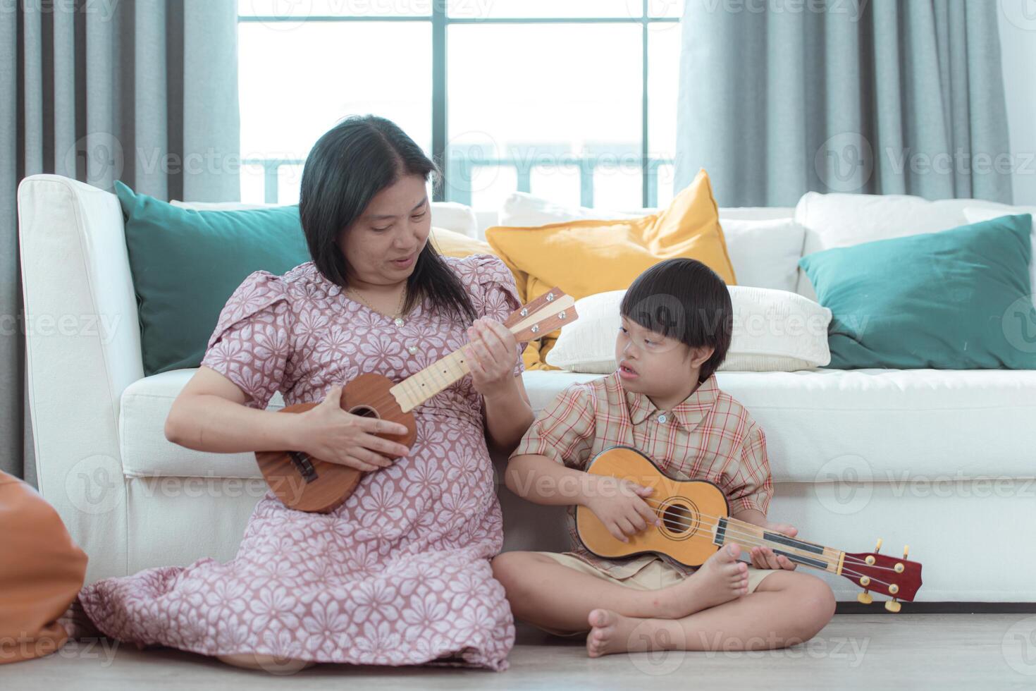 A special child with his mom plays the ukulele in the living room of the house photo