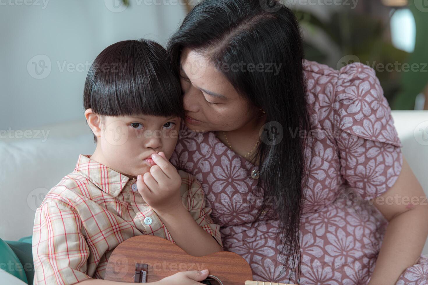 A special child with his mom plays the ukulele in the living room of the house photo