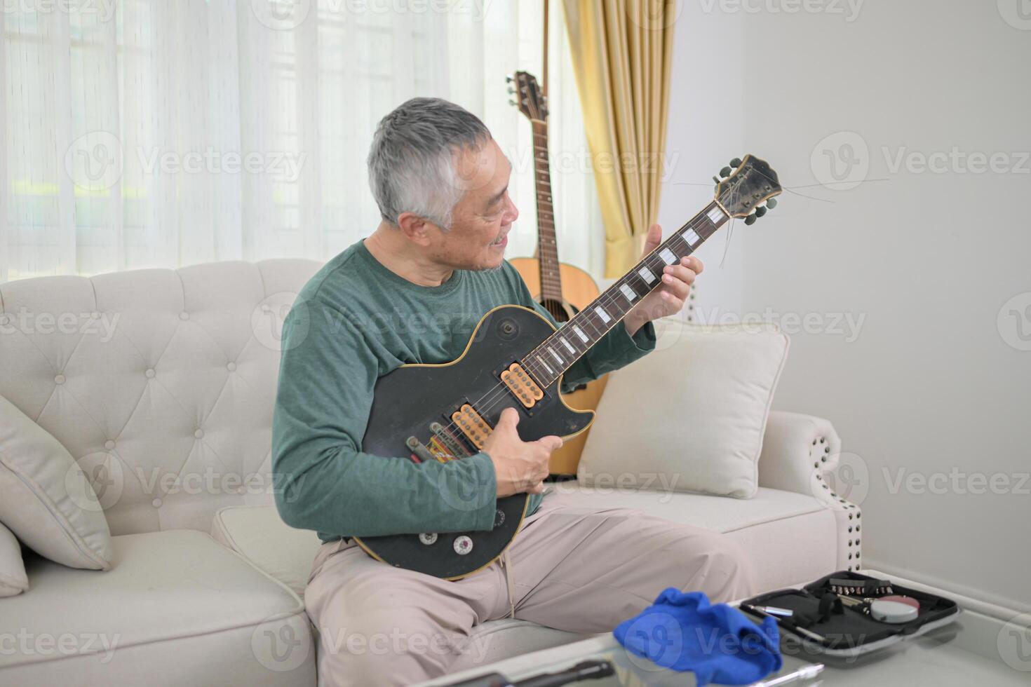 Senior man a veteran guitarist clean and repair the old electric guitar at home photo