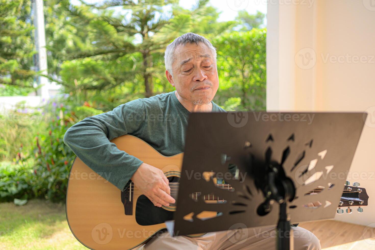 Senior man a veteran guitarist plays music in the garden at home photo