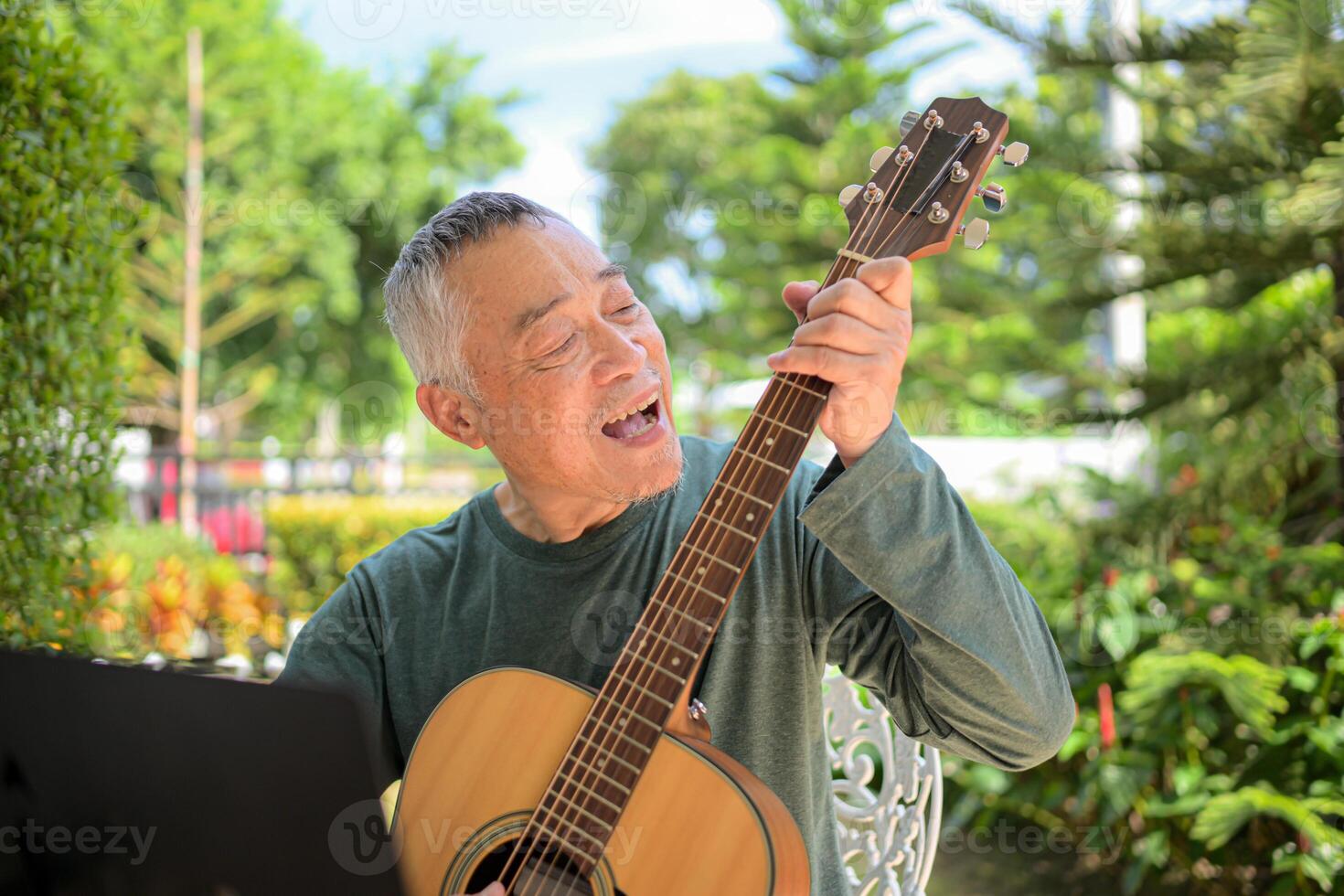 Senior man a veteran guitarist plays music in the garden at home photo