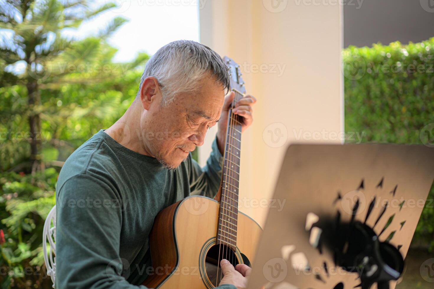 Senior man a veteran guitarist plays music in the garden at home photo