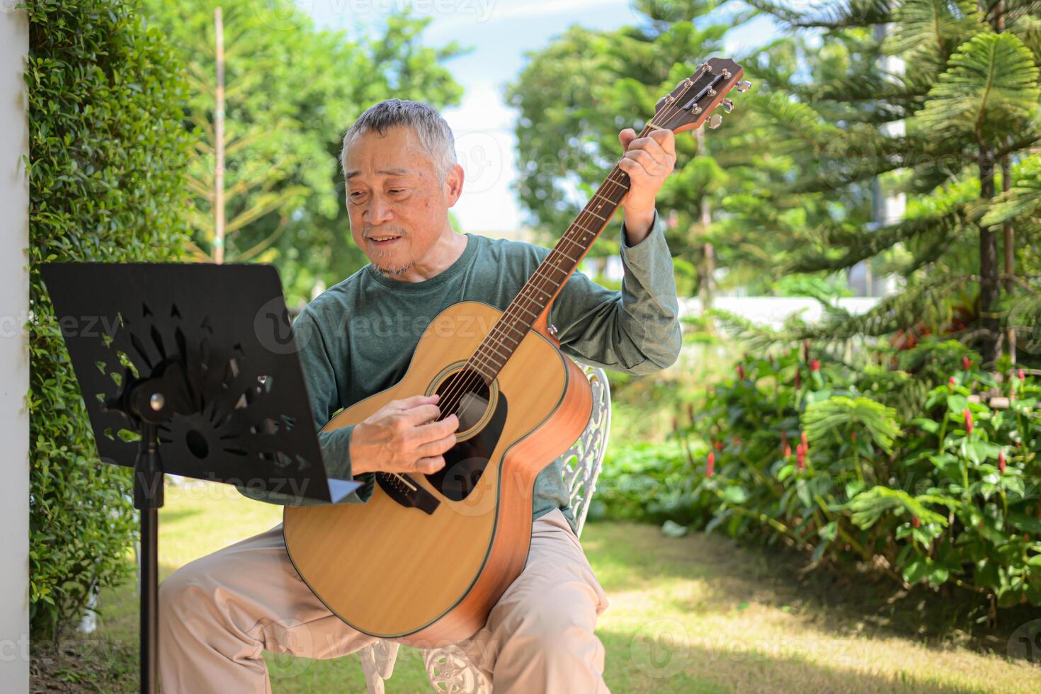 Senior man a veteran guitarist plays music in the garden at home photo