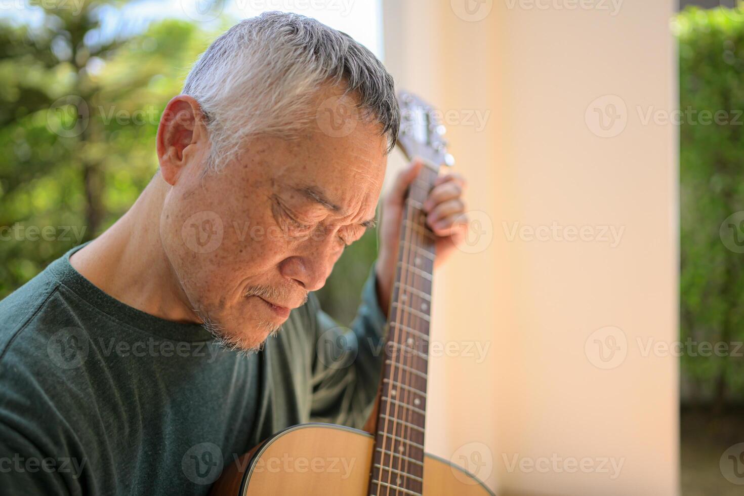 Senior man a veteran guitarist plays music in the garden at home photo