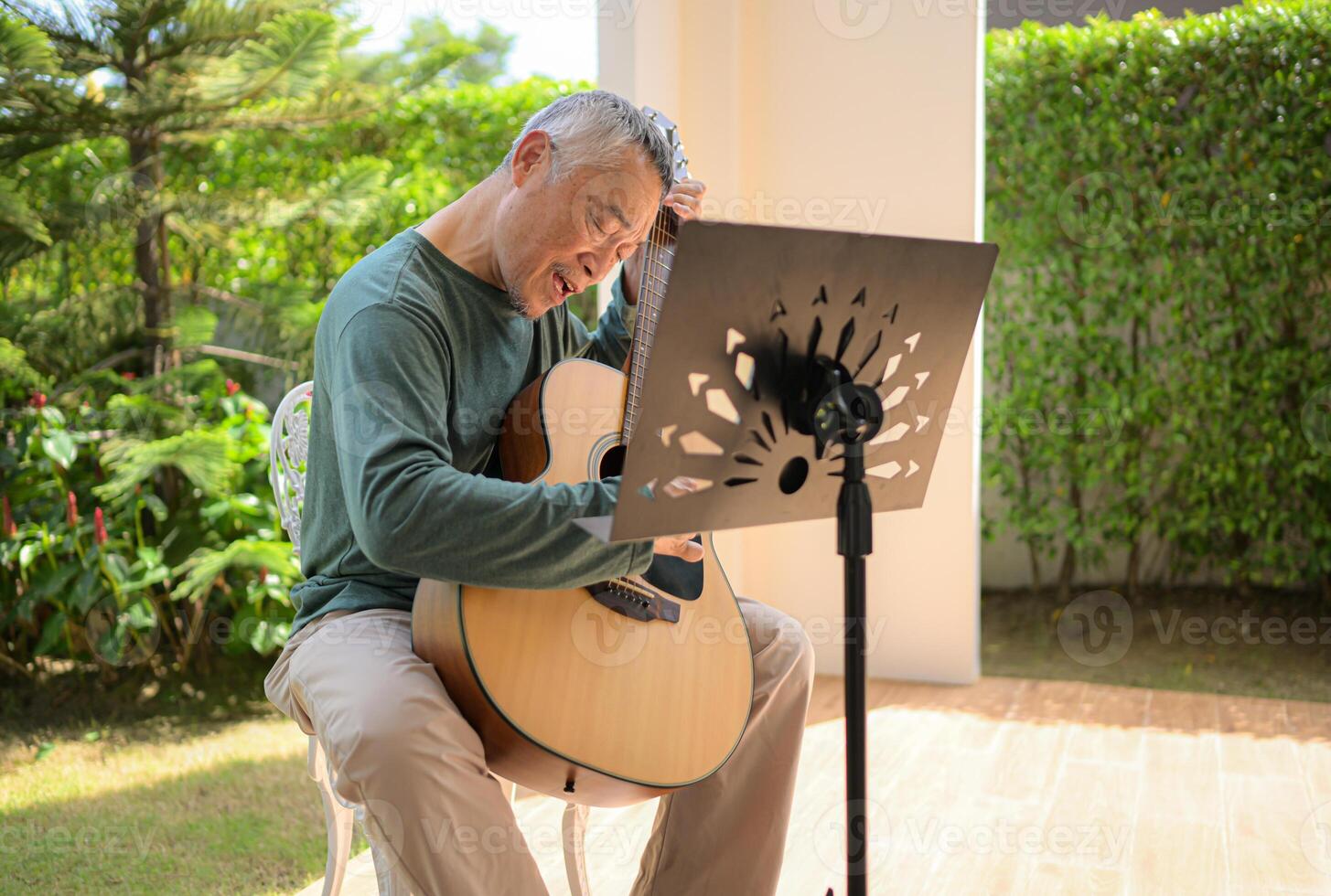 Senior man a veteran guitarist plays music in the garden at home photo