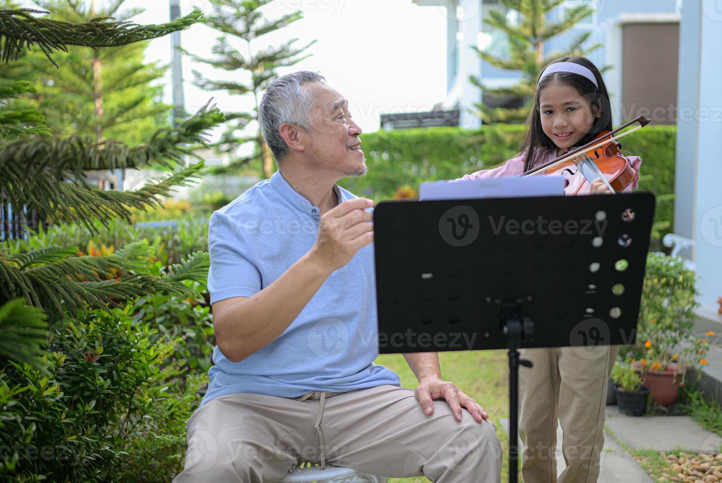 A girl violinist and her grandfather practice music together in the garden at home photo