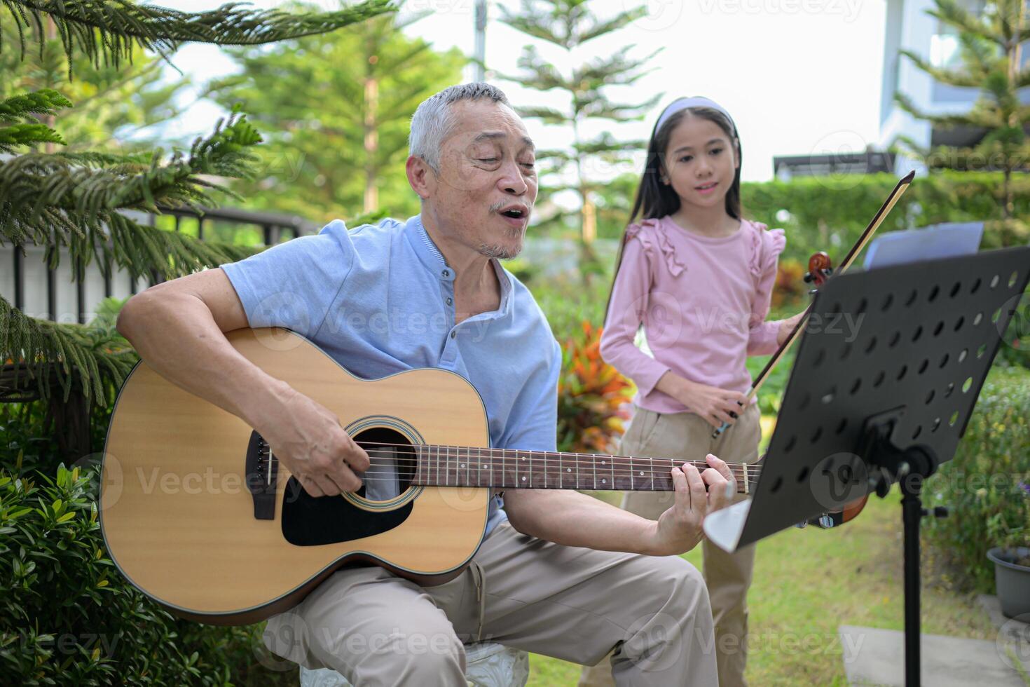 A girl violinist and her grandfather practice music together in the garden at home photo
