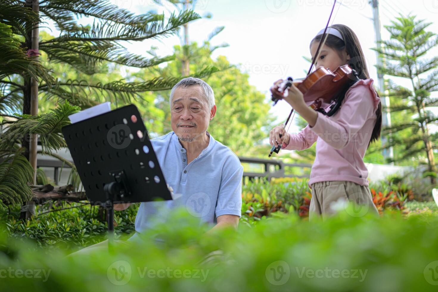 A girl violinist and her grandfather practice music together in the garden at home photo