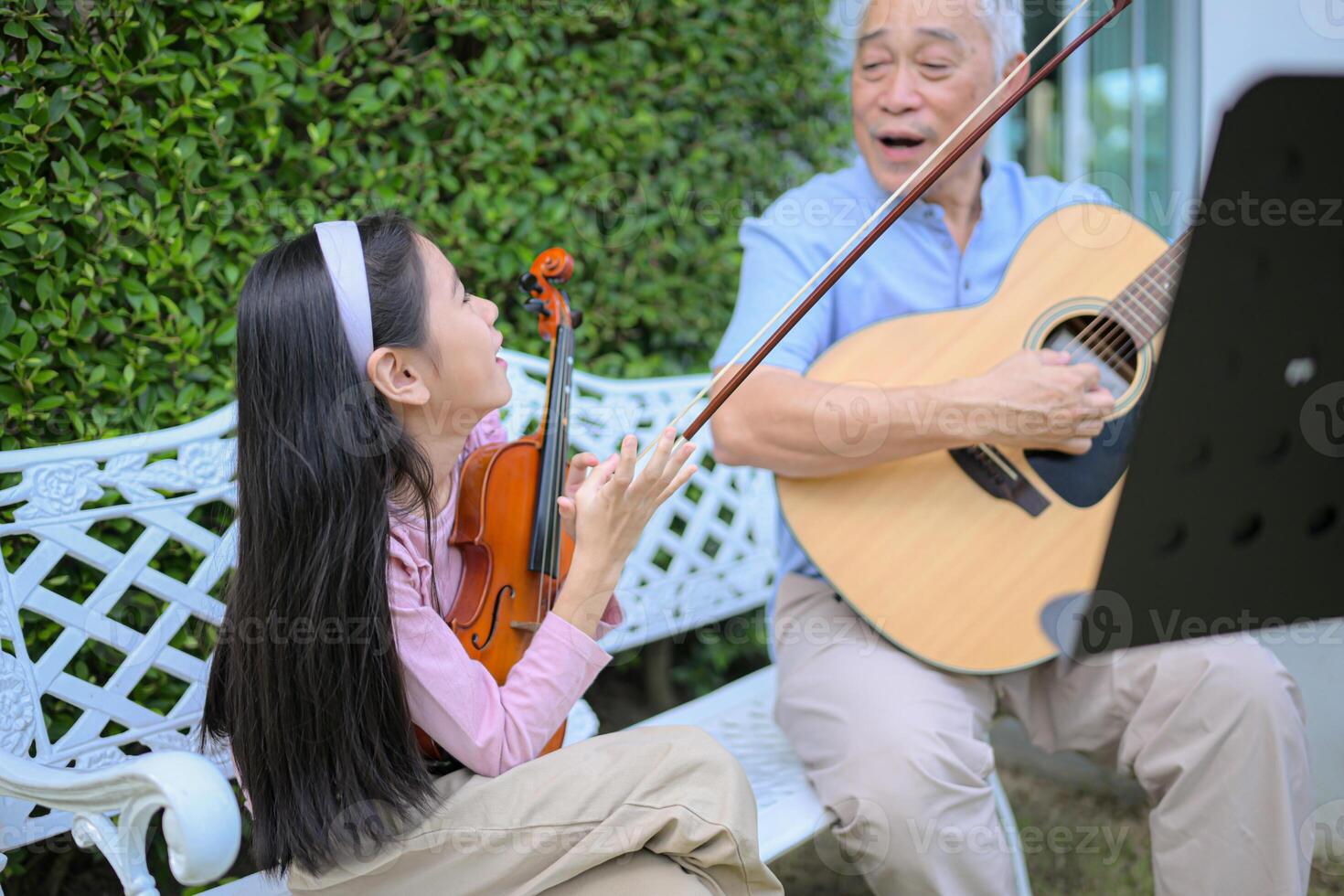 A girl violinist and her grandfather practice music together in the garden at home photo