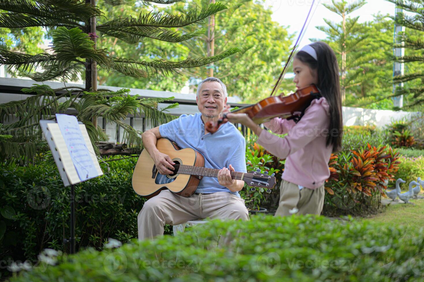 A girl violinist and her grandfather practice music together in the garden at home photo