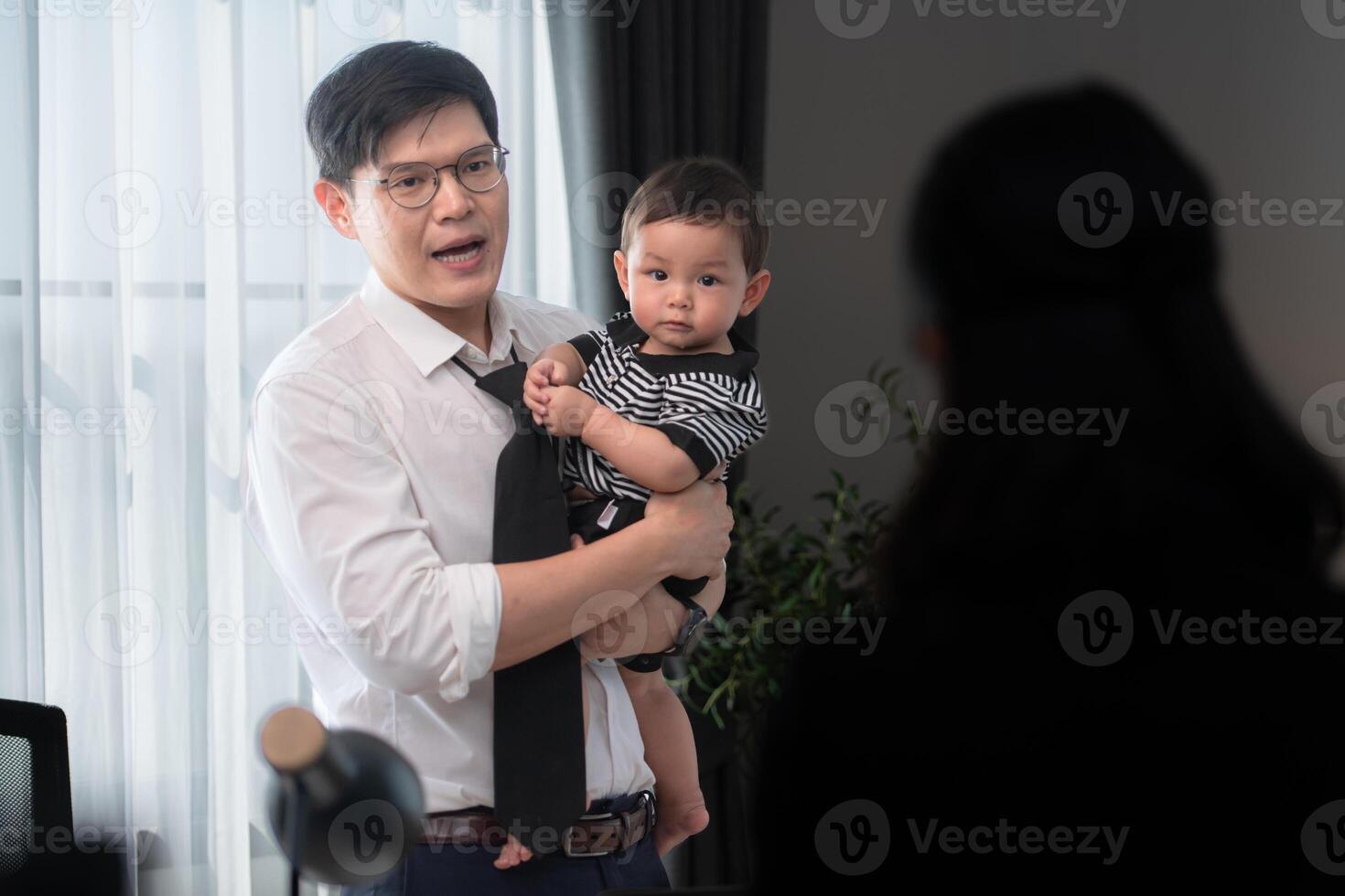 A business father assigns work to his secretary, while also taking care of his child while working photo
