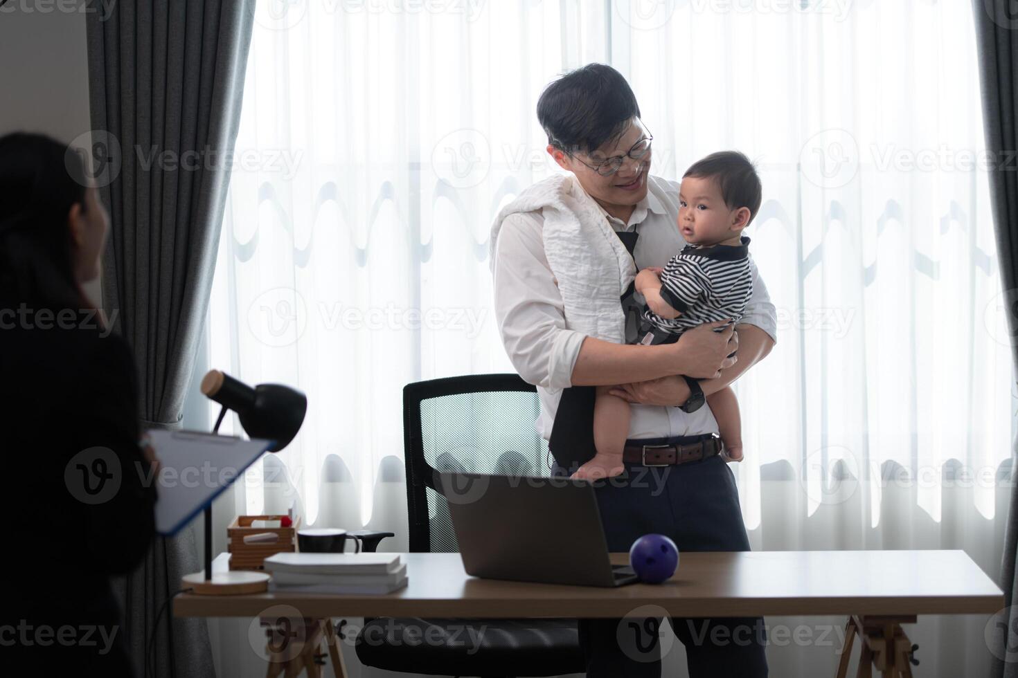 A business father assigns work to his secretary, while also taking care of his child while working photo