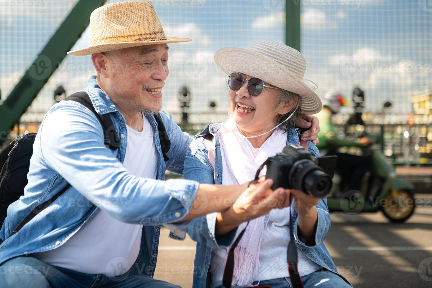 An elderly couple relaxes and looks at photos in camera after walking through the city streets with the road and bridge structures in the background