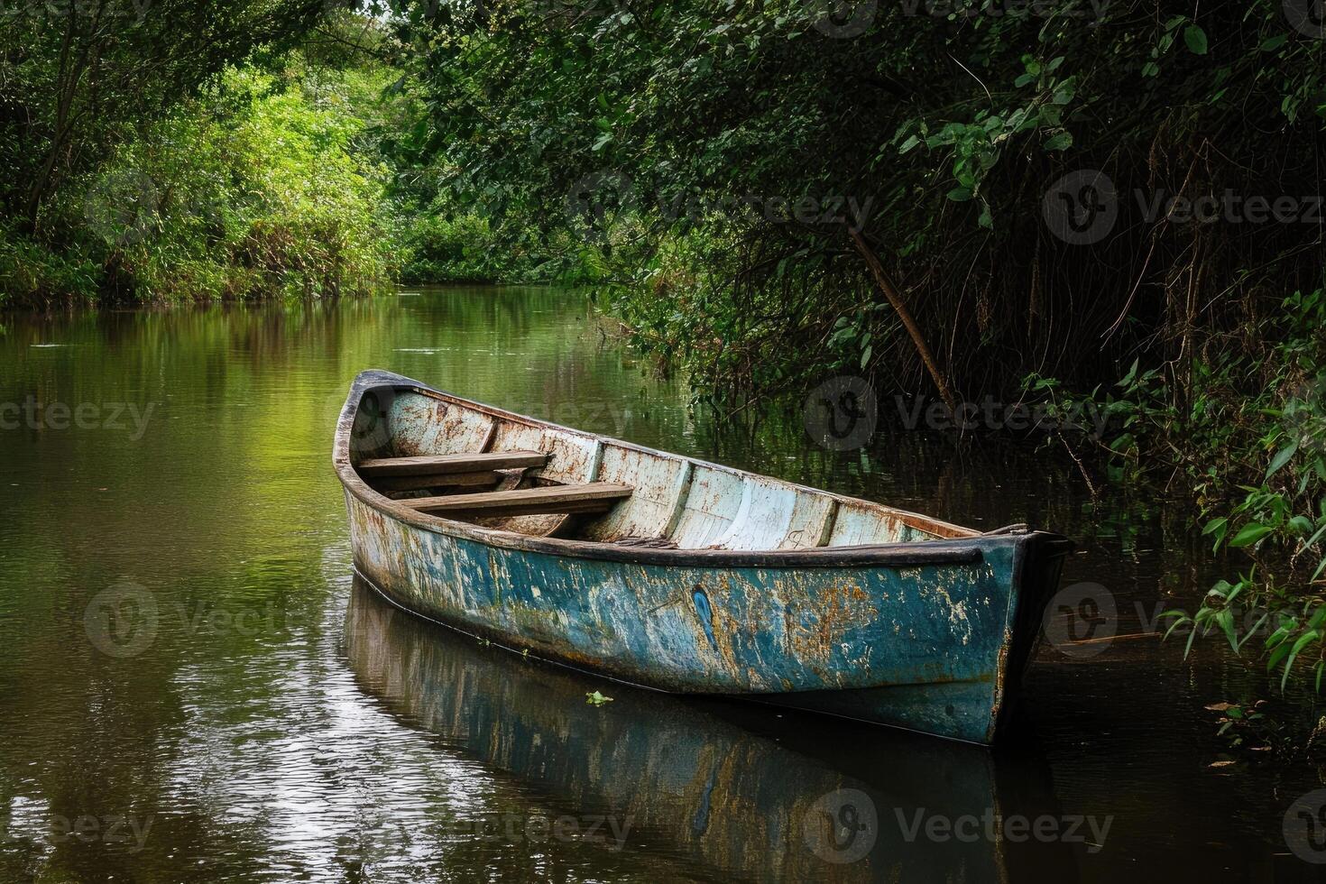 A weathered wooden rowboat rests in a still river, surrounded by lush green foliage. photo