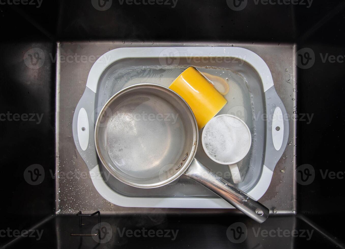 Dirty dishes in a sink basin with hot water and foam from an environmental oxygen cleaner. A modern product for removing dirt and stains. photo