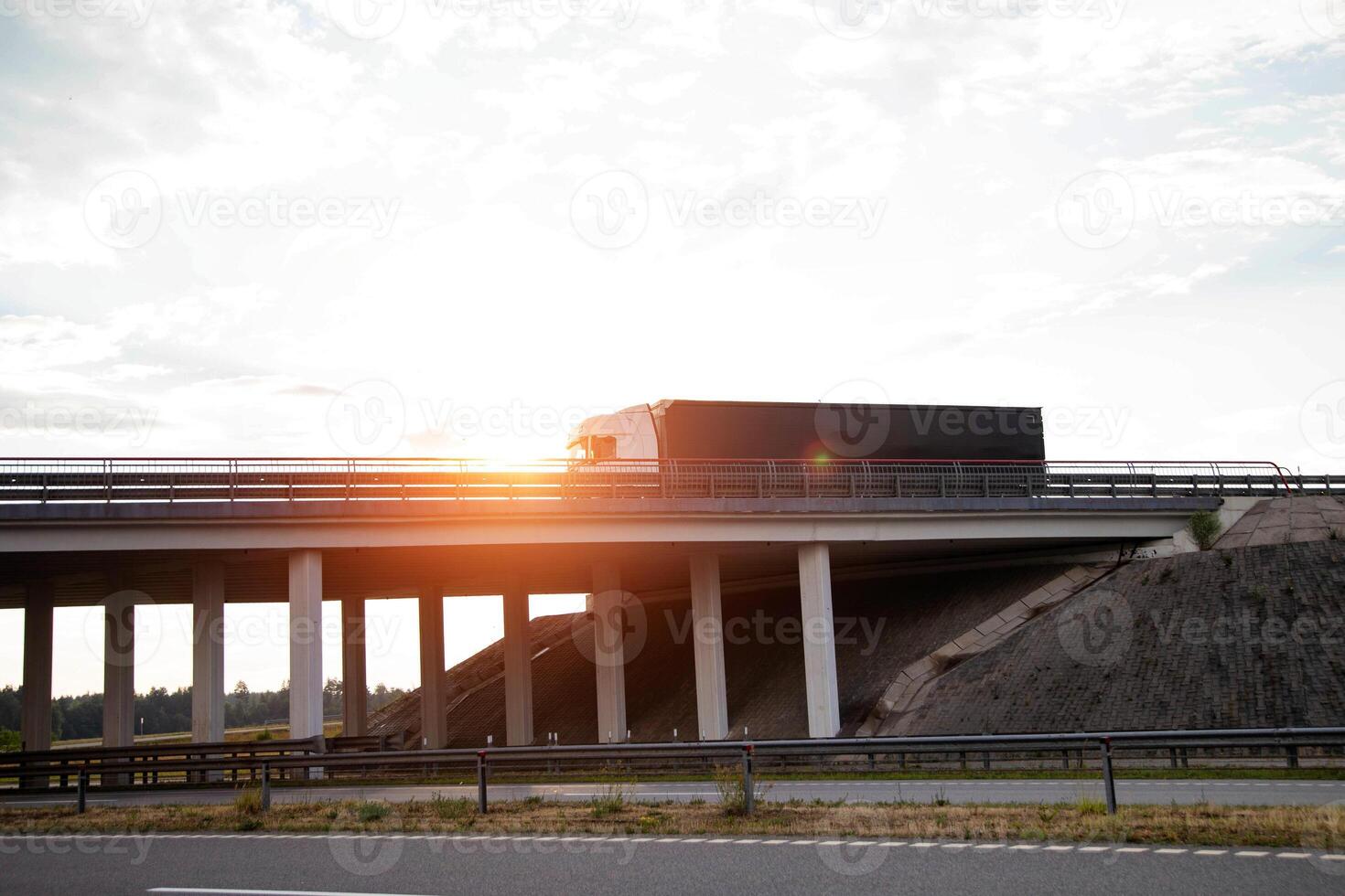 A truck with a curtain-sided semi-trailer transports a load of construction materials in the evening along a bridge photo