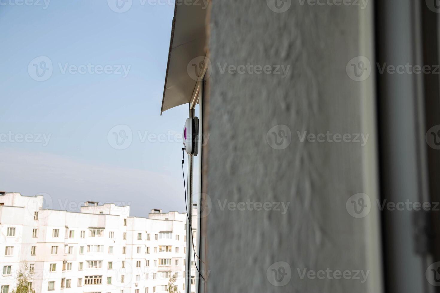 A modern vacuum robot window washer washes glass in an apartment on a balcony. View outside from the street. Safety from falls from a height. photo