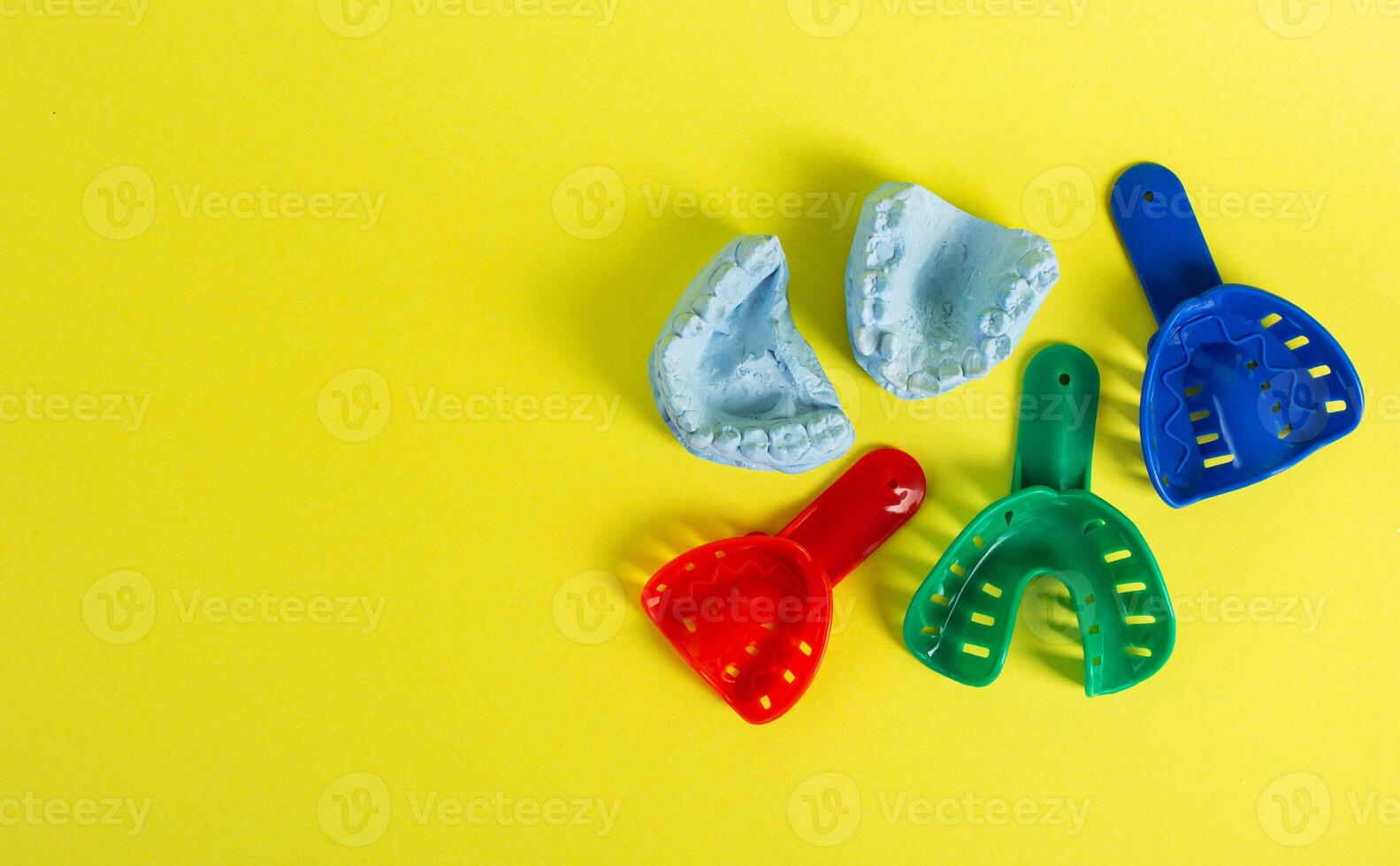 Blue plaster cast of a dental jaw and a dental tray for an impression of a dental jaw on a yellow background. The concept of orthodontics in dentistry, the manufacture of dentures and crowns. photo