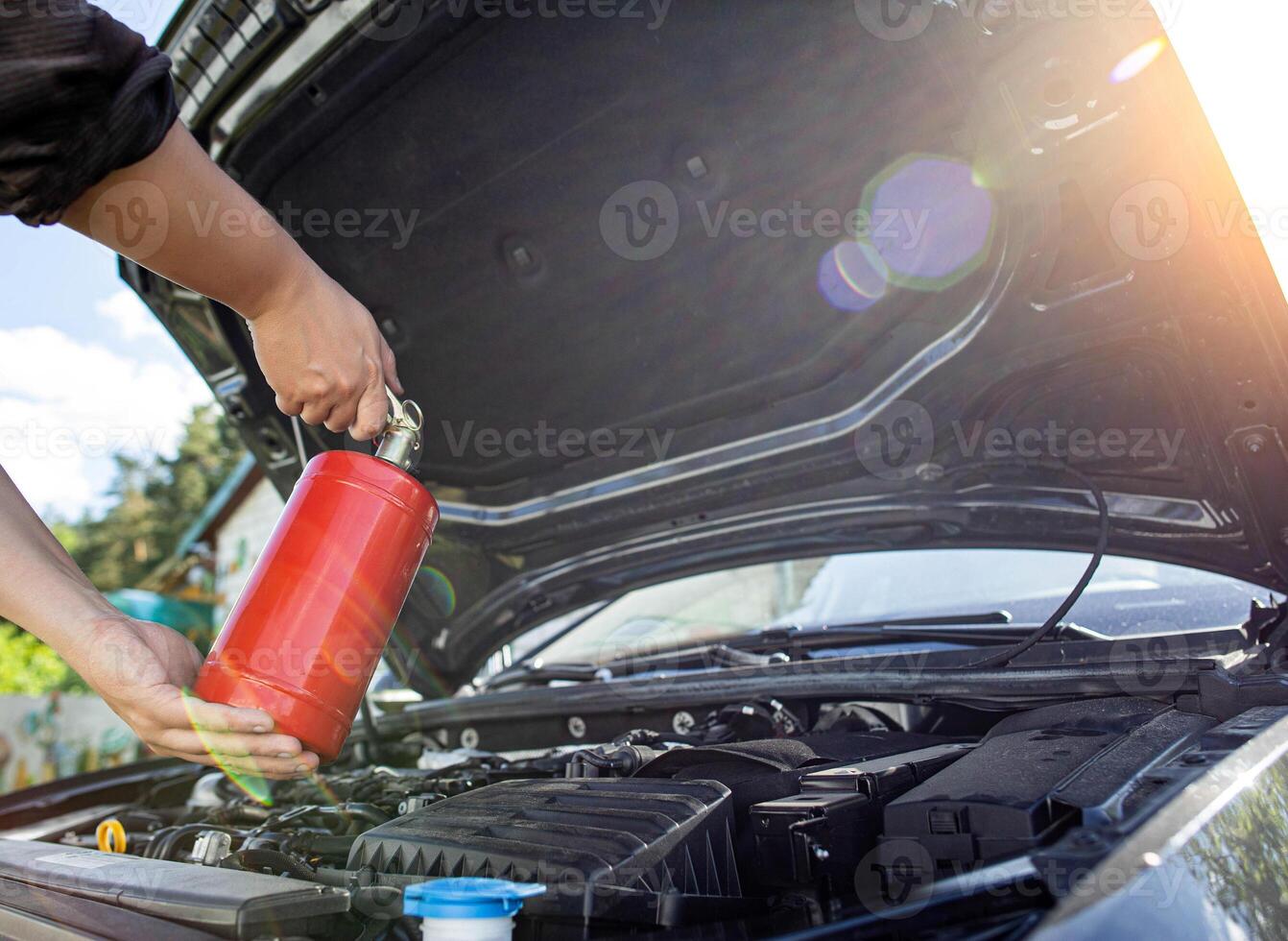 The driver of the car directs a powder fire extinguisher at the engine compartment of the car in which there is fire and smoke. Car fire, background. Electrical short circuit photo