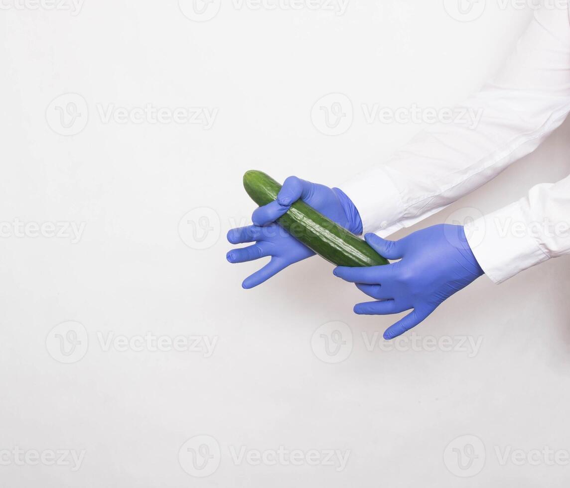 The doctor in medical gloves holds a cucumber in his hands, the concept of increasing the penis with the help of massage techniques and techniques, white background, copy space photo