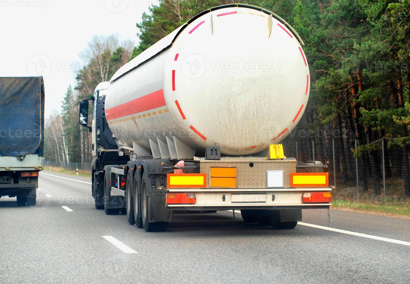 A truck with a semi-trailer tanker transports a dangerous chemical cargo of acid and alkali along a country road in the spring, industry photo