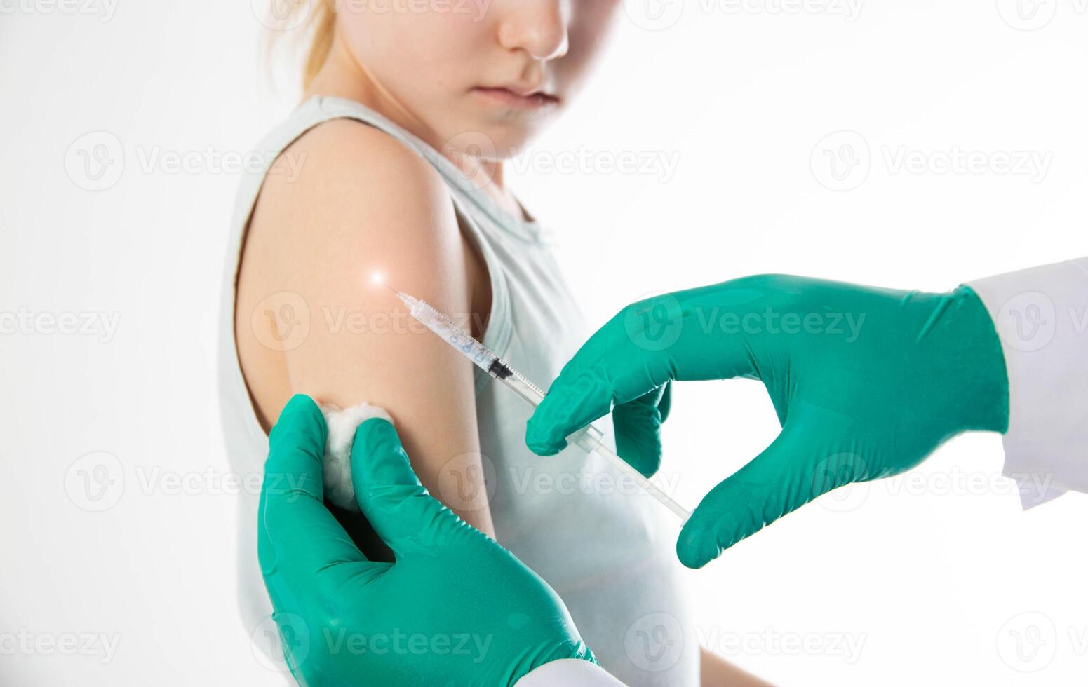 The hands of a doctor in green medical gloves make a vaccination against diphtheria, whooping cough and tetanus in the shoulder of a child girl. Copy space for text, revaccination photo