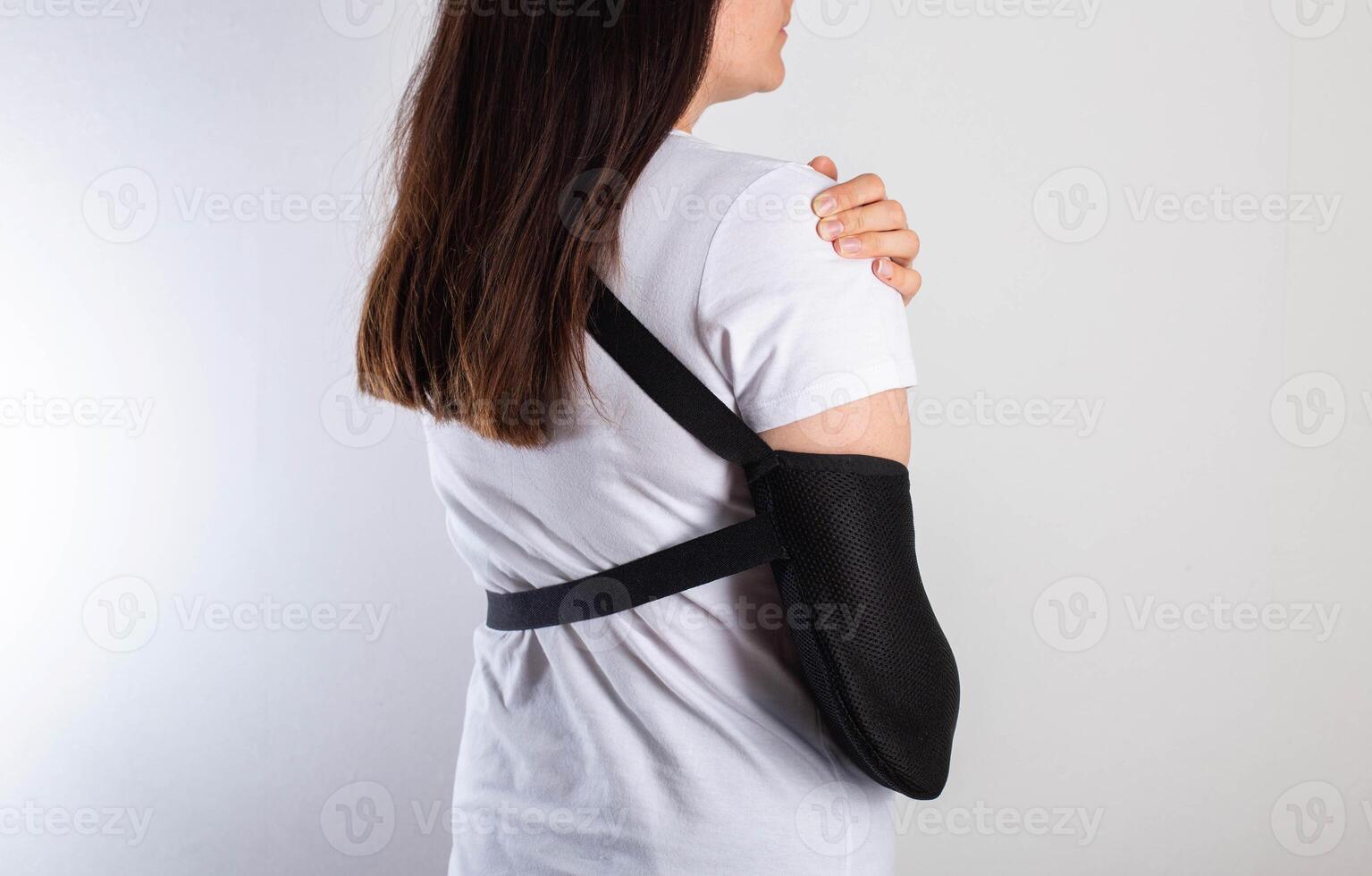 A girl on a white background with a black supporting medical bandage after a dislocation of the shoulder joint and a bone fracture. Rehabilitation after injury, orthopedics and traumatology photo