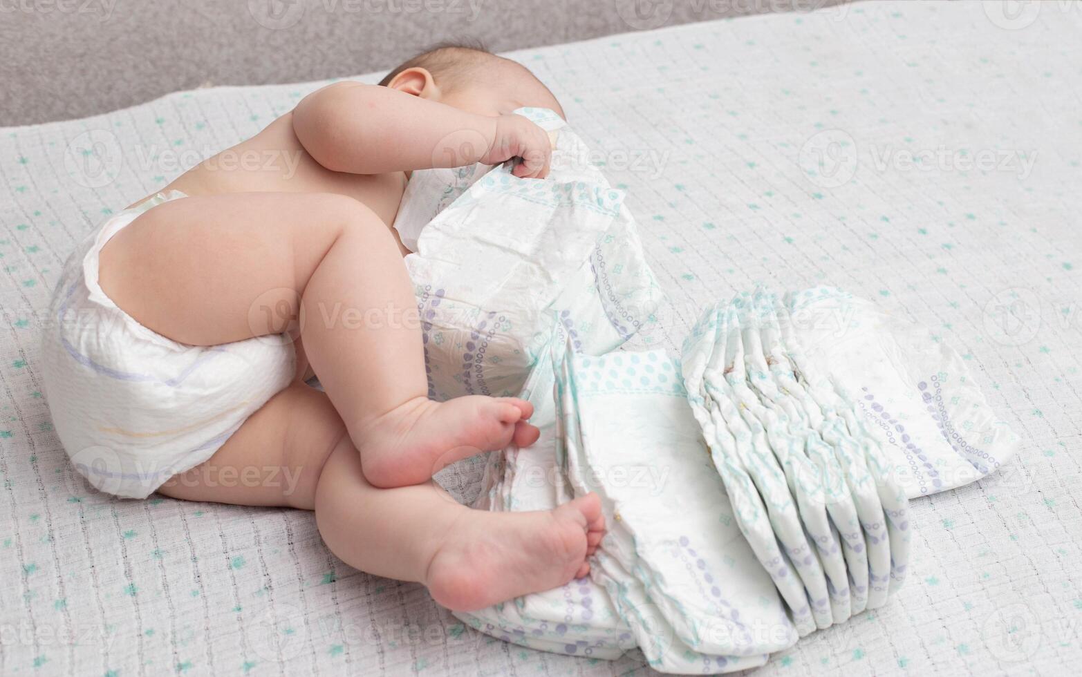 A little caucasian baby boy in a diaper lies on a white background and plays with a bunch of diapers. Copy space for text photo