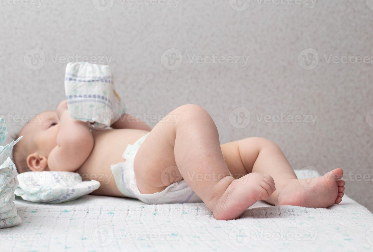 A baby in a diaper lies on a white background plays with a stack of diapers. Copy space for text photo
