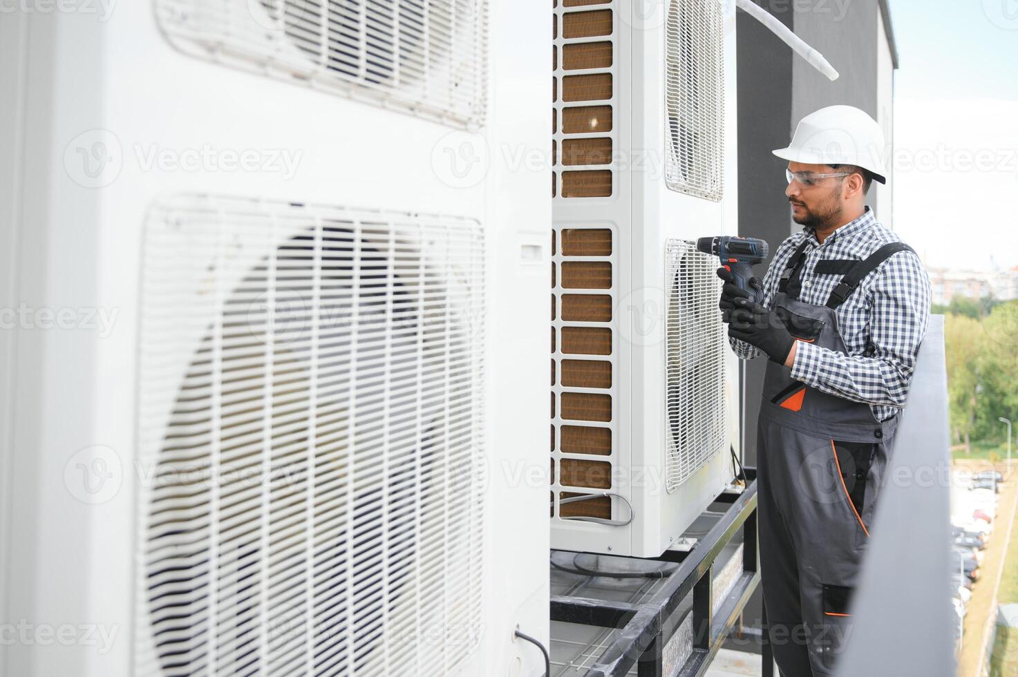 Indian Repairman in uniform installing the outside unit of air conditioner photo