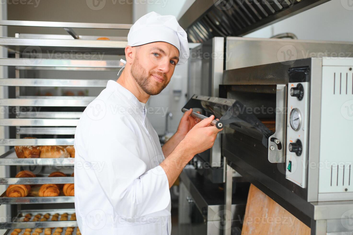 Portrait of handsome baker at the bakery with breads and oven on the background photo