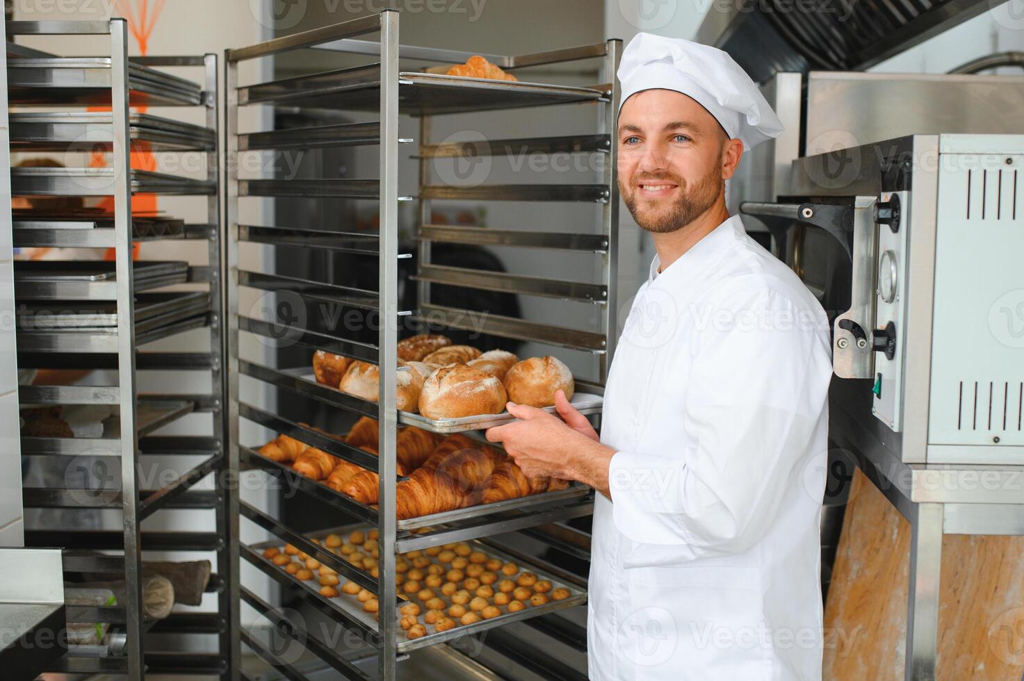Male baker holding a tray of baked breads in bakery shop photo
