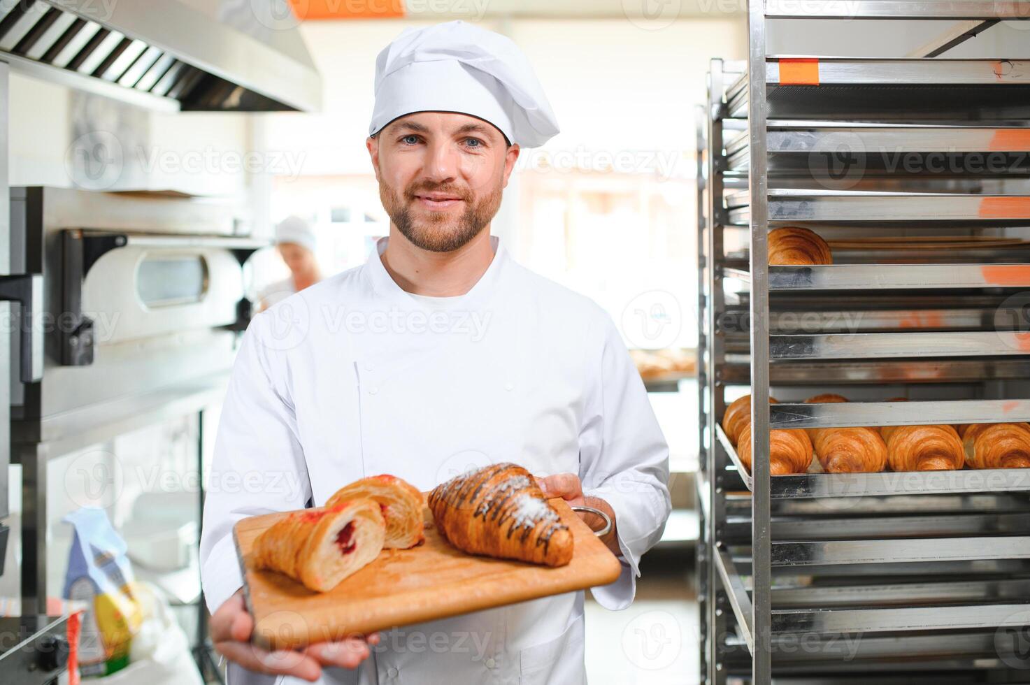 A young handsome male baker holds a tray with French croissants in front of a bakery and smiles photo
