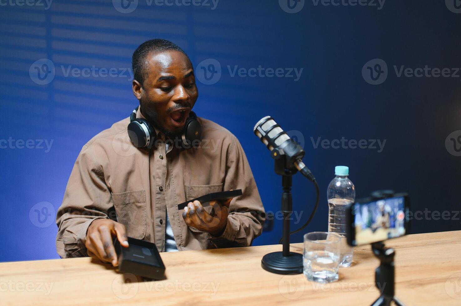 Black vlogger filming podcast on smartphone in studio. Cheerful blogger photo