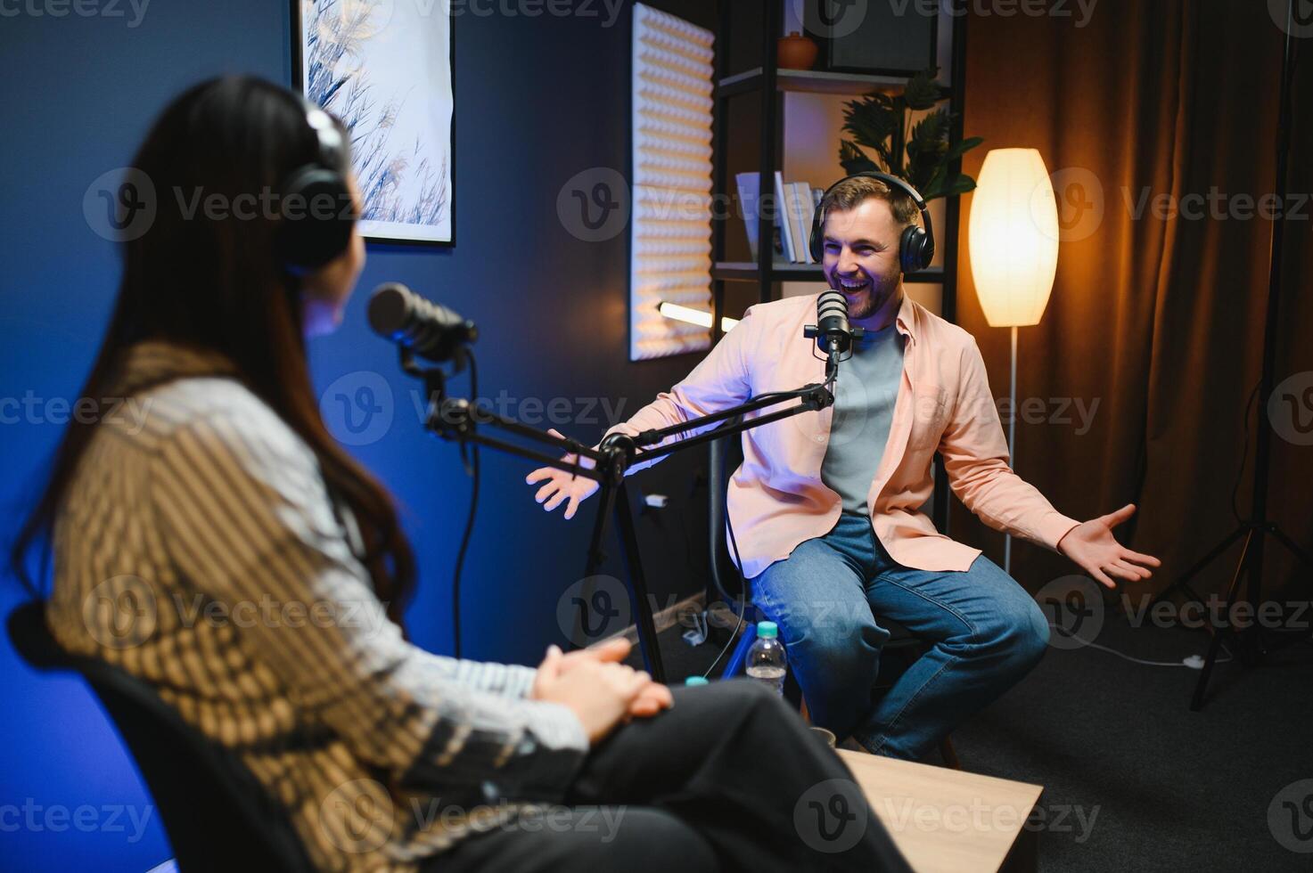 Female podcaster in headphones interviewing man guest using microphone, smiling, recording and broadcasting audio podcast in studio. Content creator, blogging photo