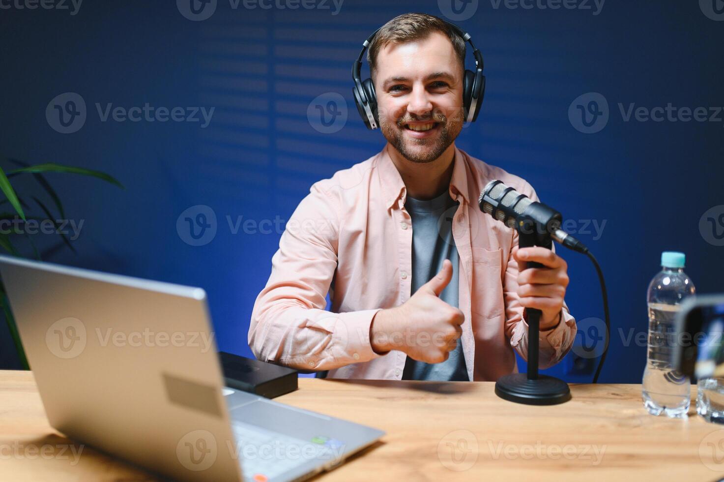 Man podcaster influencer blogger smiling while broadcasting his live audio podcast in studio using headphones. Male radio host making podcast or interview photo