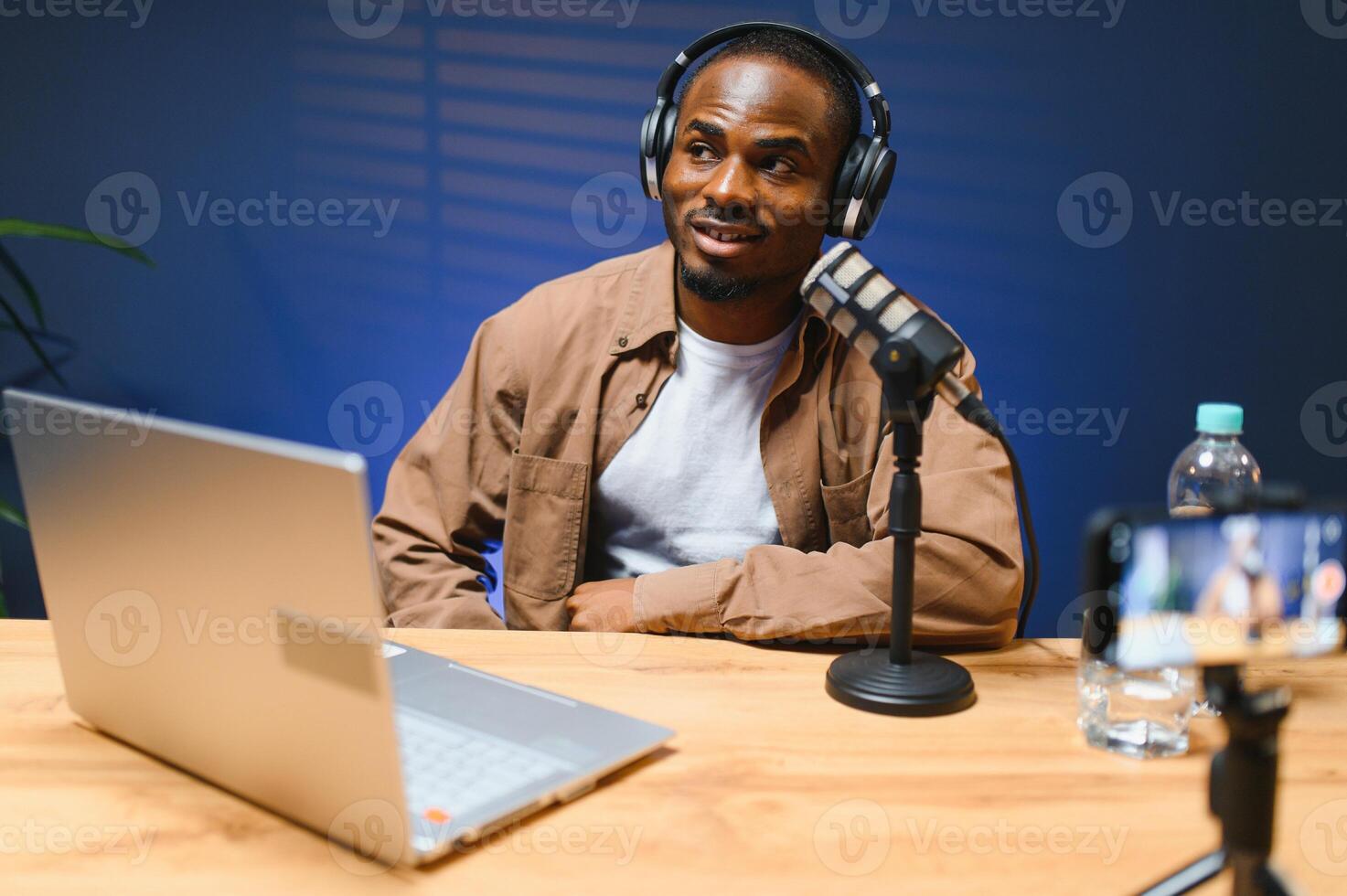 Black vlogger filming podcast on smartphone in studio. Cheerful blogger photo