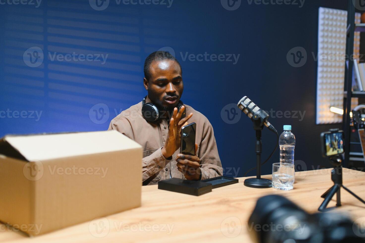 Black vlogger filming podcast on smartphone in studio. Cheerful blogger photo