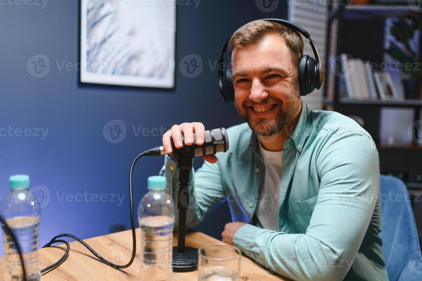 Man podcaster influencer blogger smiling while broadcasting his live audio podcast in studio using headphones. Male radio host making podcast or interview photo