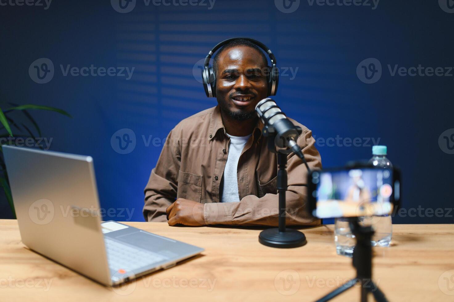 Black vlogger filming podcast on smartphone in studio. Cheerful blogger photo