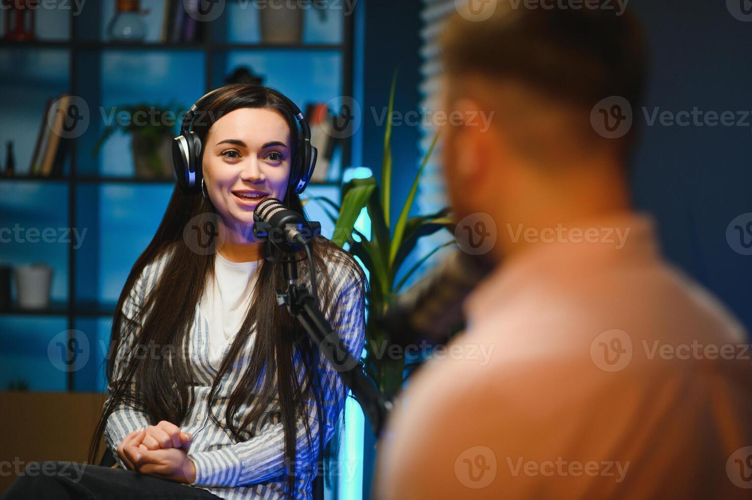 Female podcaster in headphones interviewing man guest using microphone, smiling, recording and broadcasting audio podcast in studio. Content creator, blogging photo