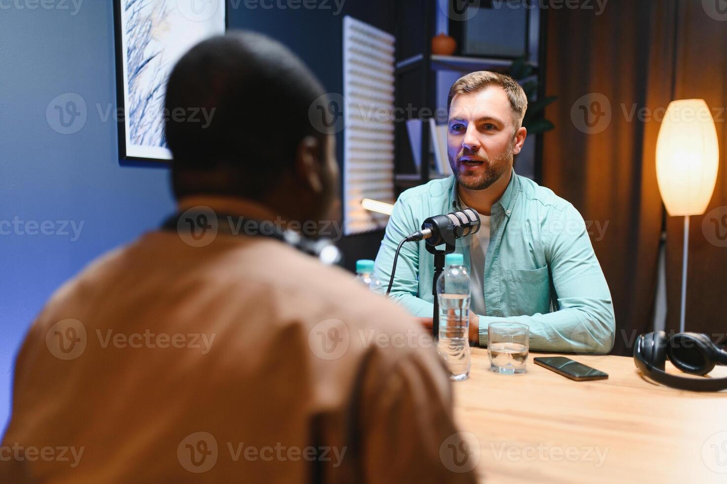 Man podcaster influencer blogger smiling while broadcasting his live audio podcast in studio using headphones. Male radio host making podcast or interview photo