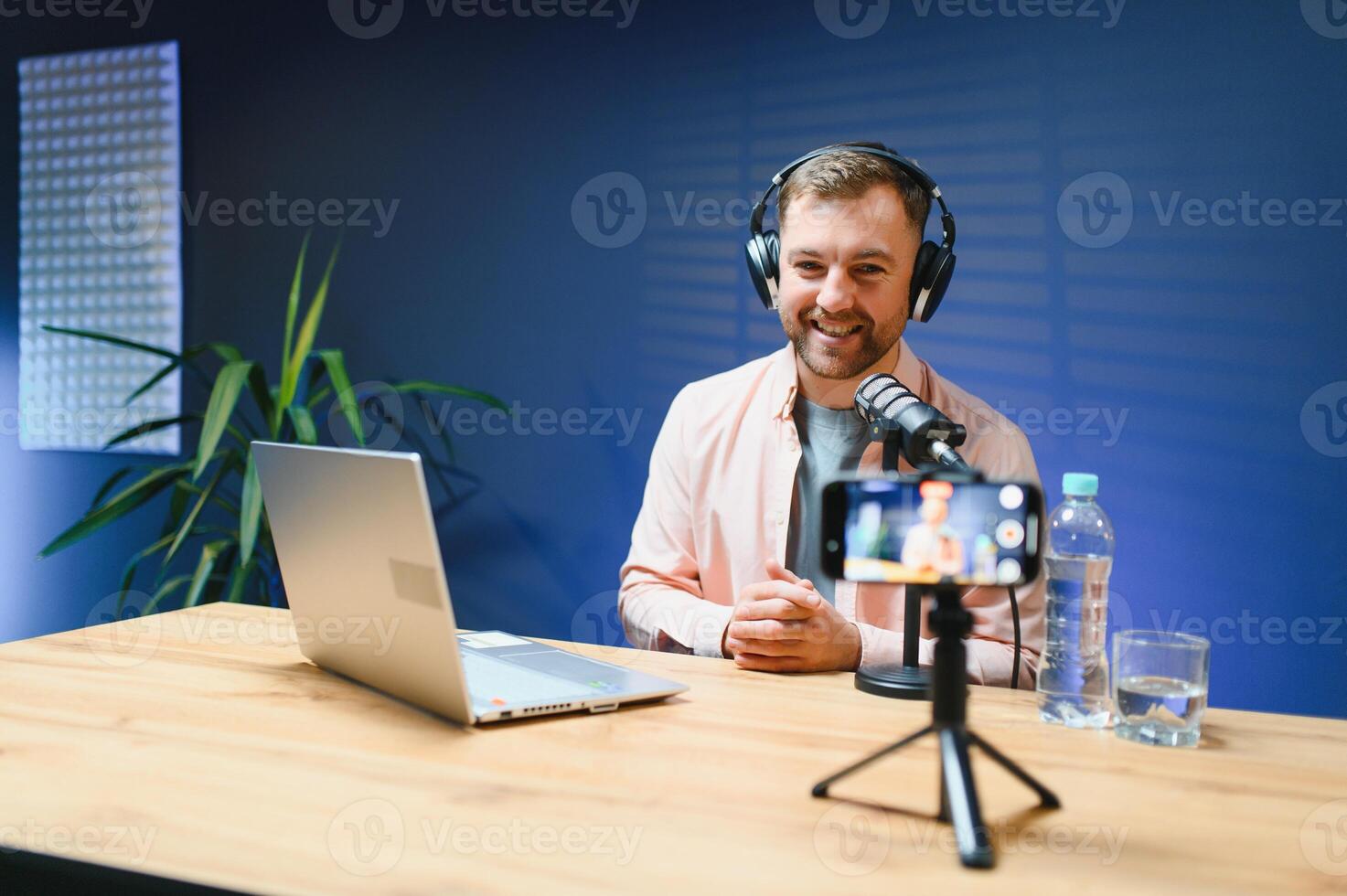 Man podcaster influencer blogger smiling while broadcasting his live audio podcast in studio using headphones. Male radio host making podcast or interview photo