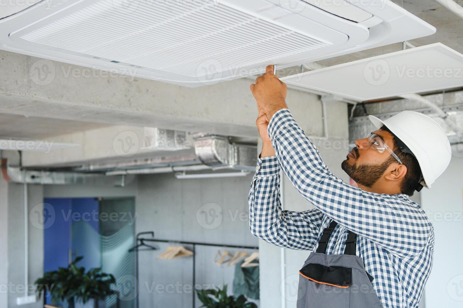 Indian male worker inspecting the air conditioner mounted on the ceiling photo