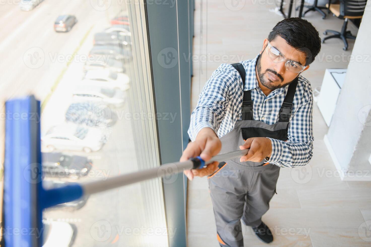 An Indian cleaning service worker washes windows in an office building photo