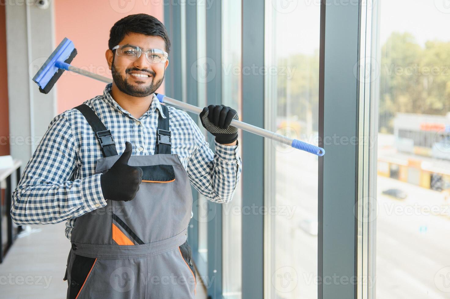 An Indian cleaning service worker washes windows in an office building photo