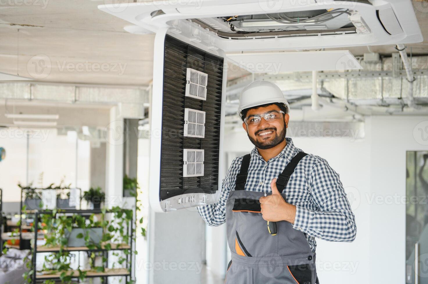 Concentrated young Indian engineer setting up air conditioner photo